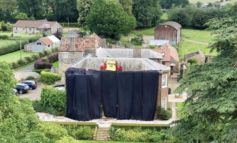 Aerial photo of a grand country house draped in black fabric. Activists on the roof hold a banner saying 'no new oil'.
