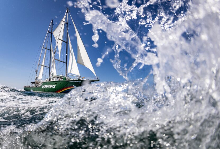 Water splashes in the foreground as a large ship sails along the sea in the background