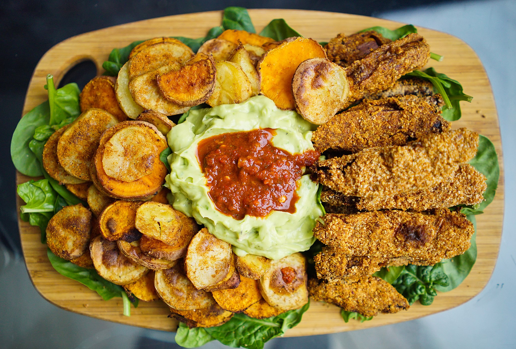 Overhead photo of a sharing platter with spiced fried potates, spinach, guacamole and salsa.