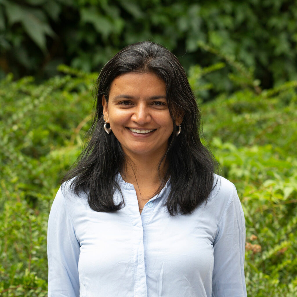 Formal portrait of Areeba smiling into the camera, with foliage in the background.