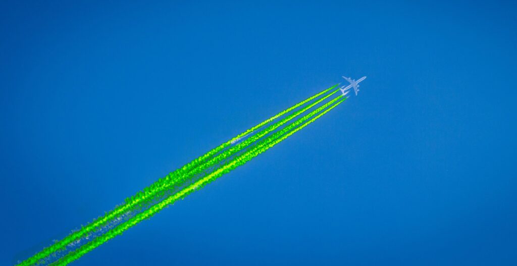 Photo illustration showing a plane flying through a clear blue sky with bright green contrails
