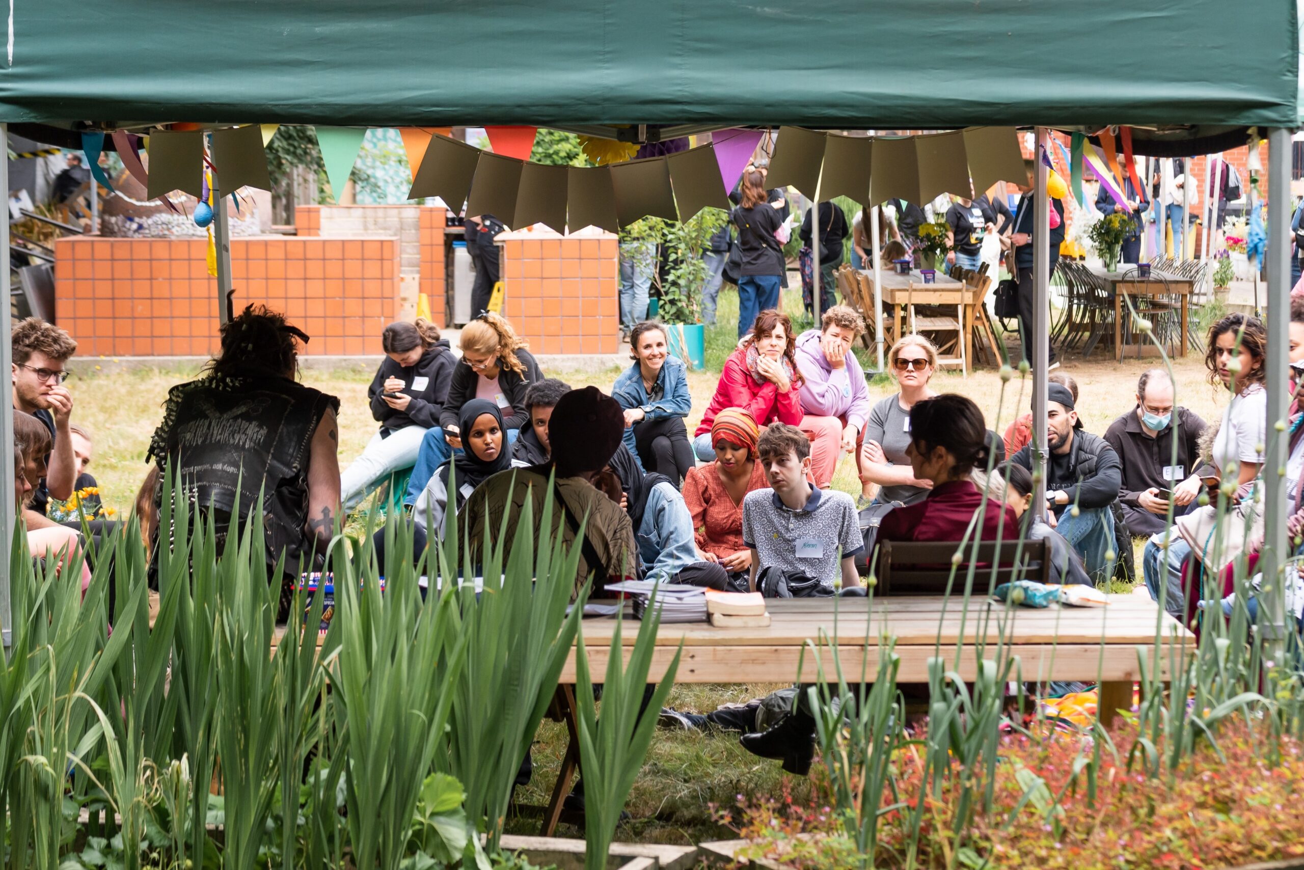 A group of people gathered under a marquee in the sunshine.