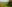 Green grassy hills dotted with trees gently slope towards a village in the distance.