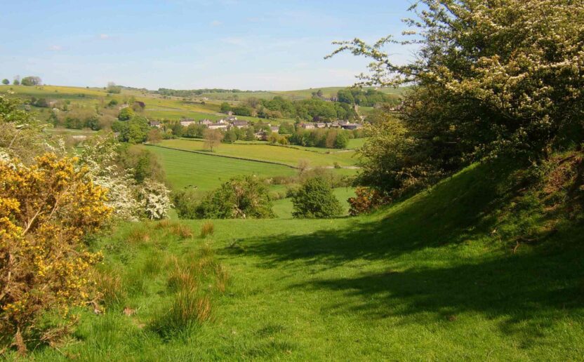 Green grassy hills dotted with trees gently slope towards a village in the distance.