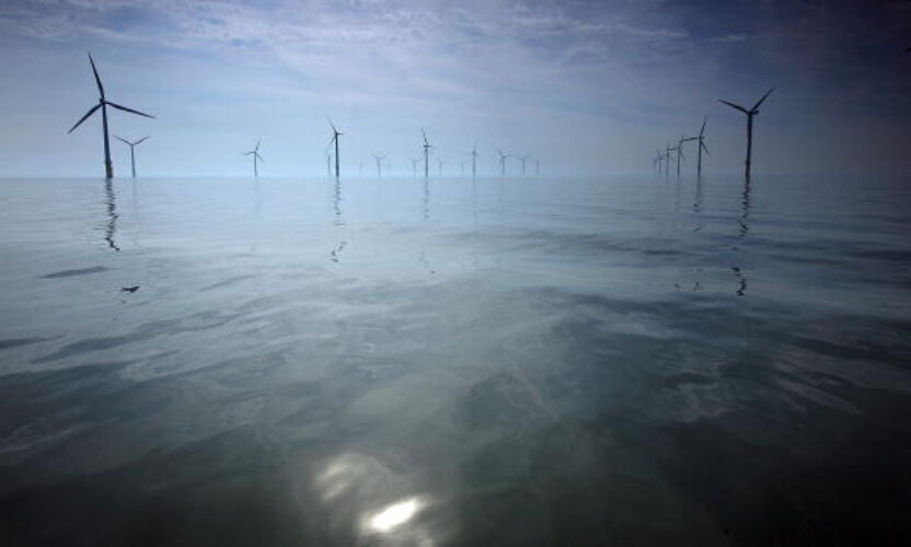 Offshore wind turbines in a reflective calm ocean with light mist