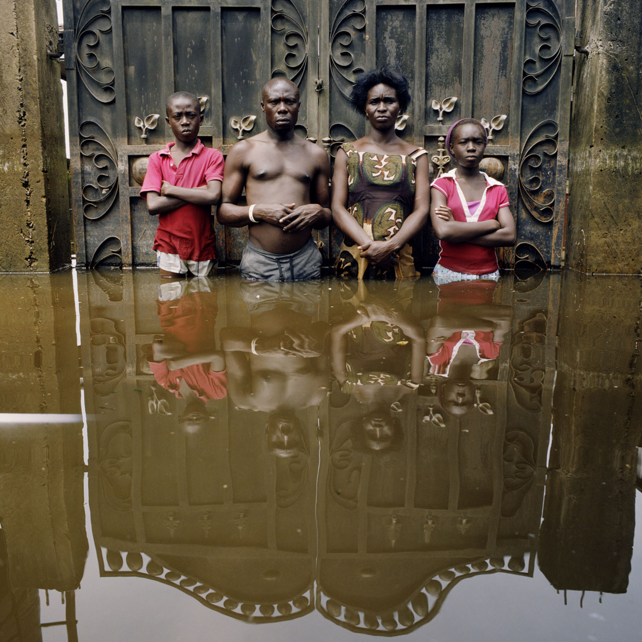 Two adults and two children stand outside an ornate gate, bottom deep in water.