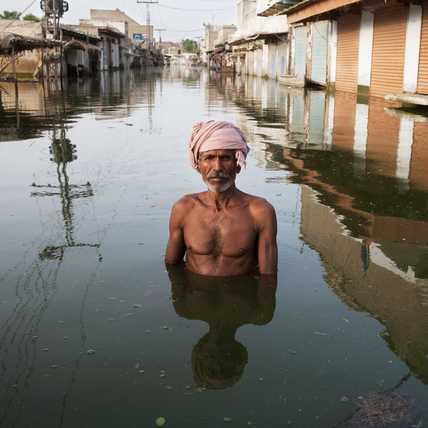 Portrait of a man standing waist-deep in water on a flooded street.
