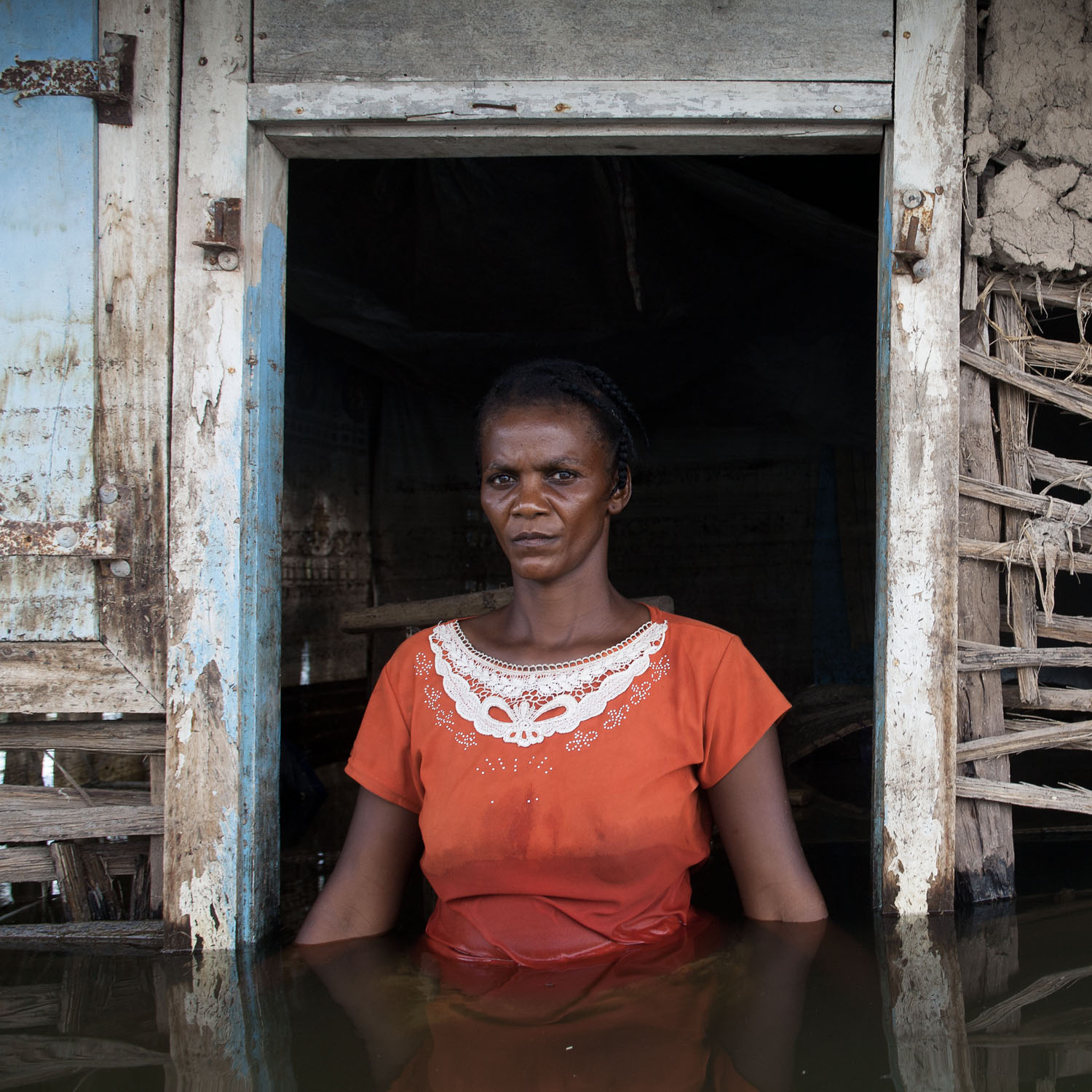 Portrait of a woman wearing orange in a doorway of a flooded house