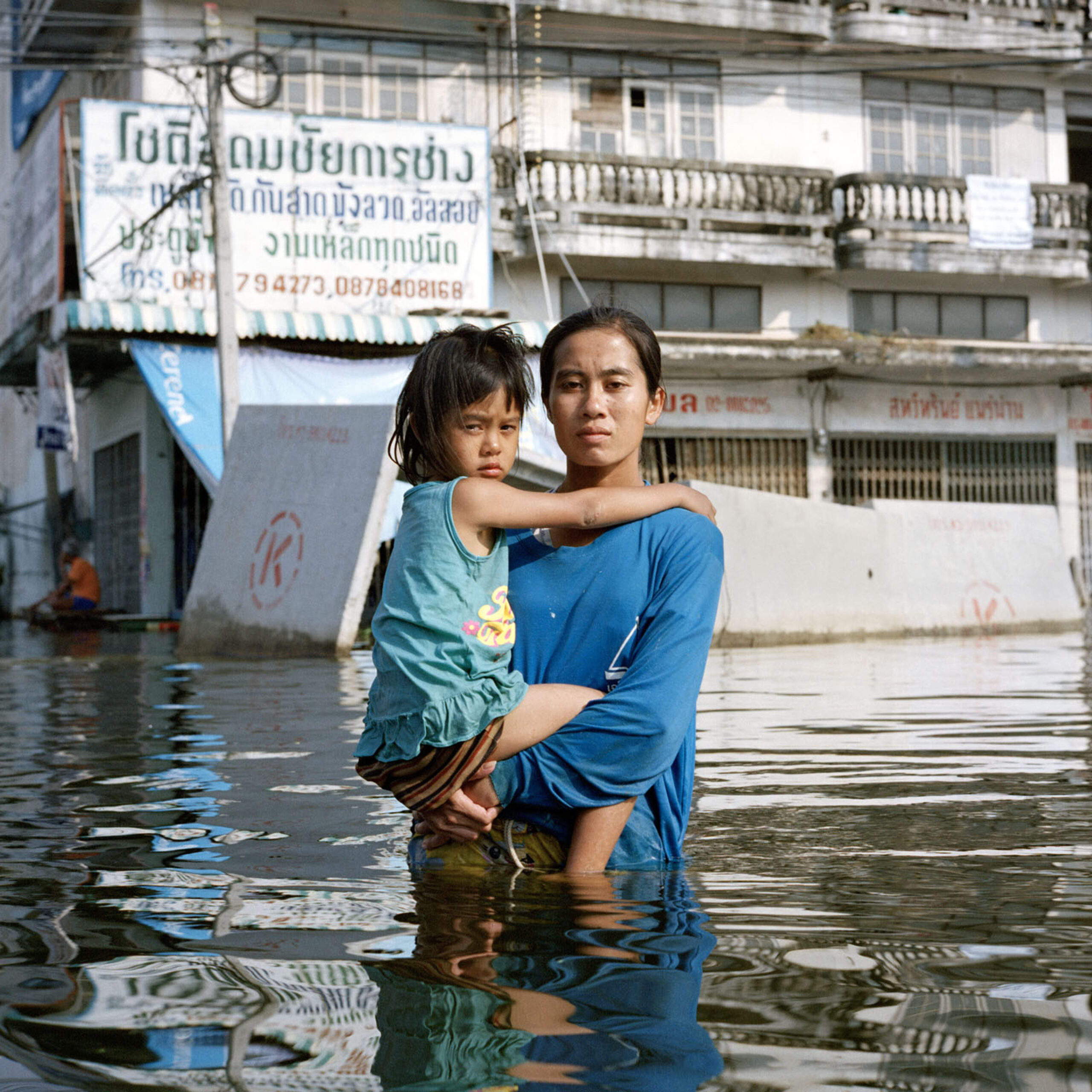 A woman holds a child, while standing hip deep on a flooded street.