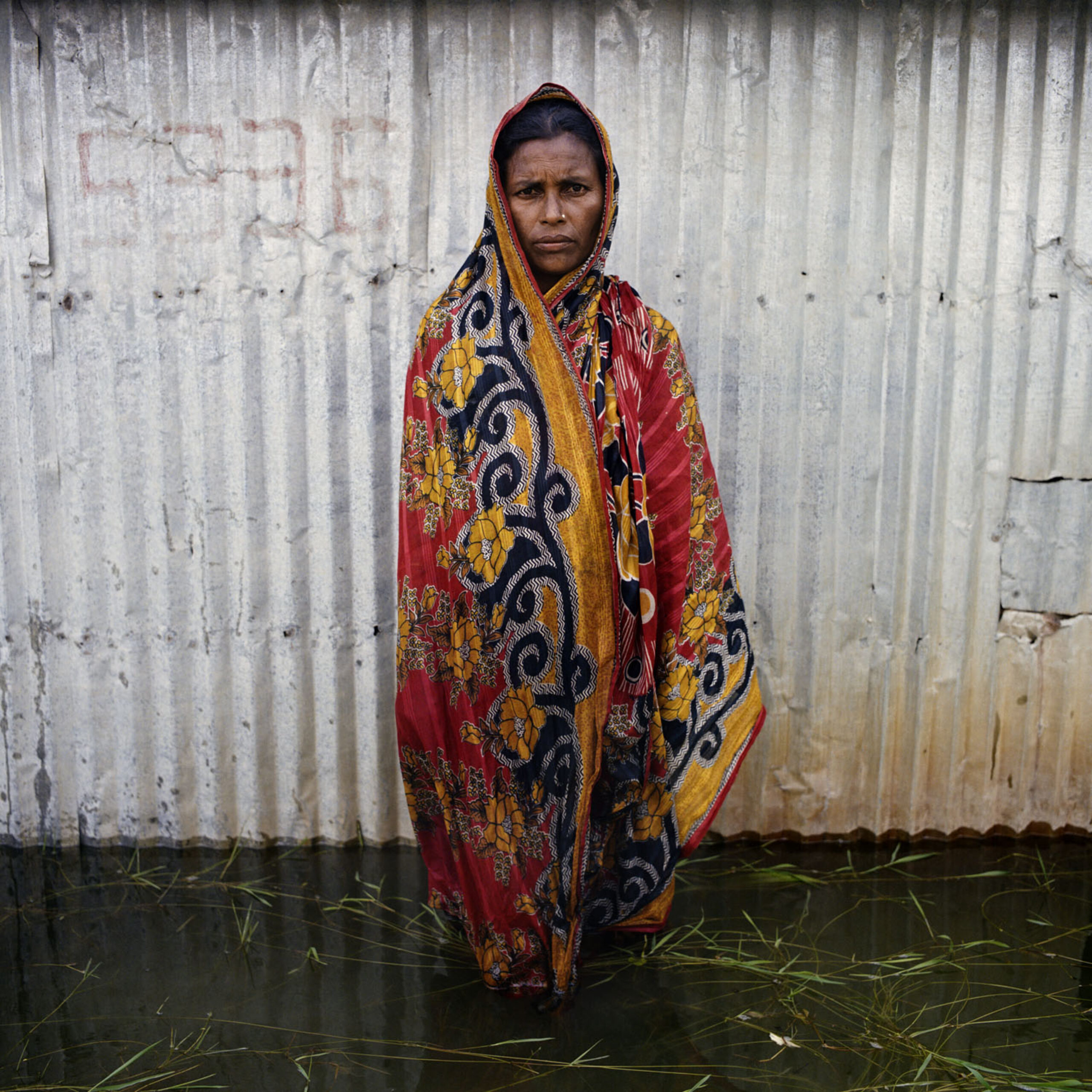 A woman in colourful fabric stands in a stark flooded street.