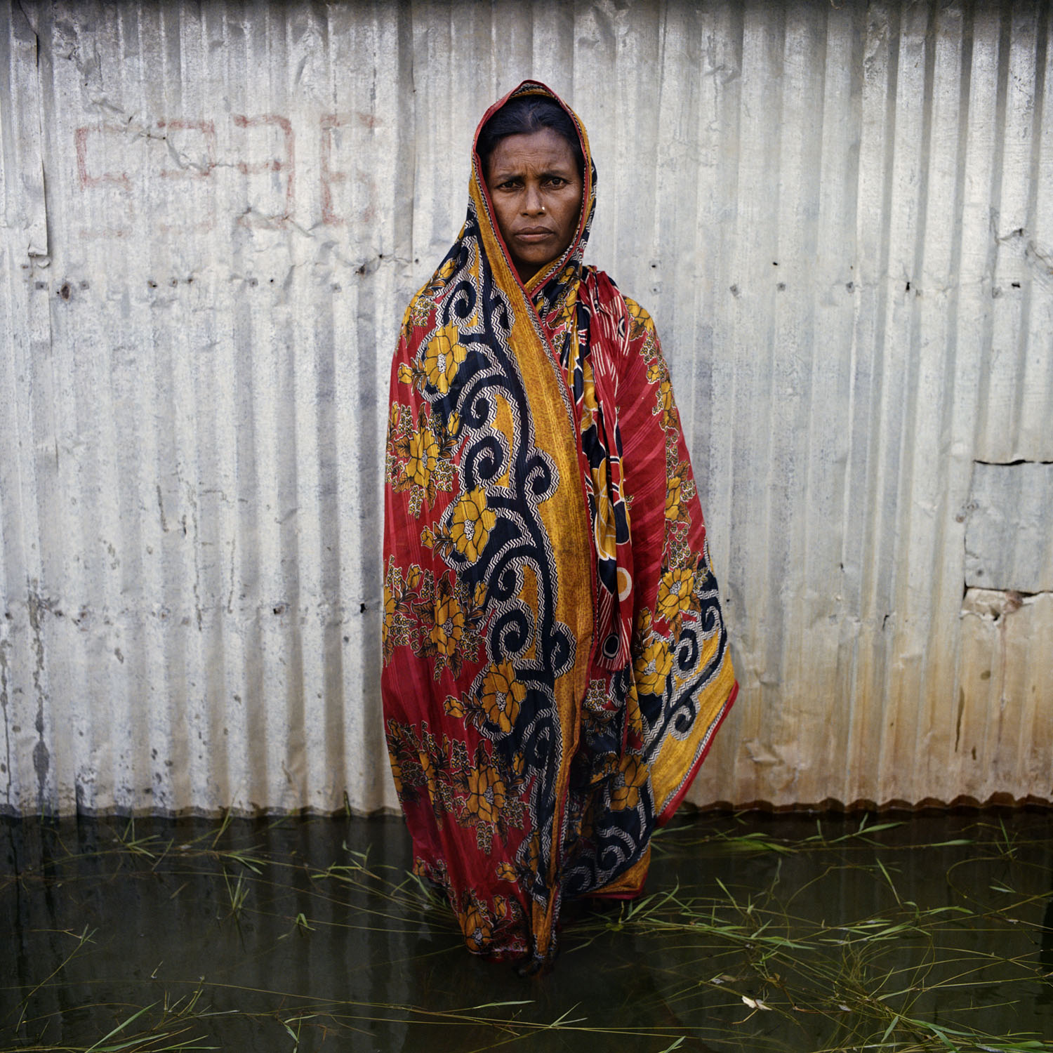 A woman in colourful fabric stands in a stark flooded street.