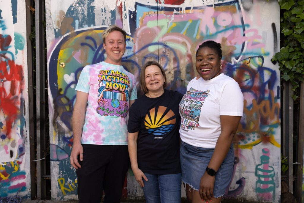 Three people of different genders and ethnicities stand in three different T-shirts from the Greenpeace festival collection