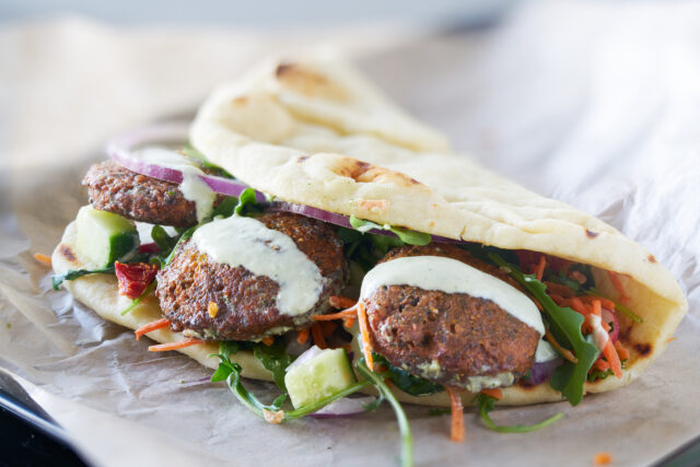 Closeup photo of falafel in a folded flatbread with sauce and salad.