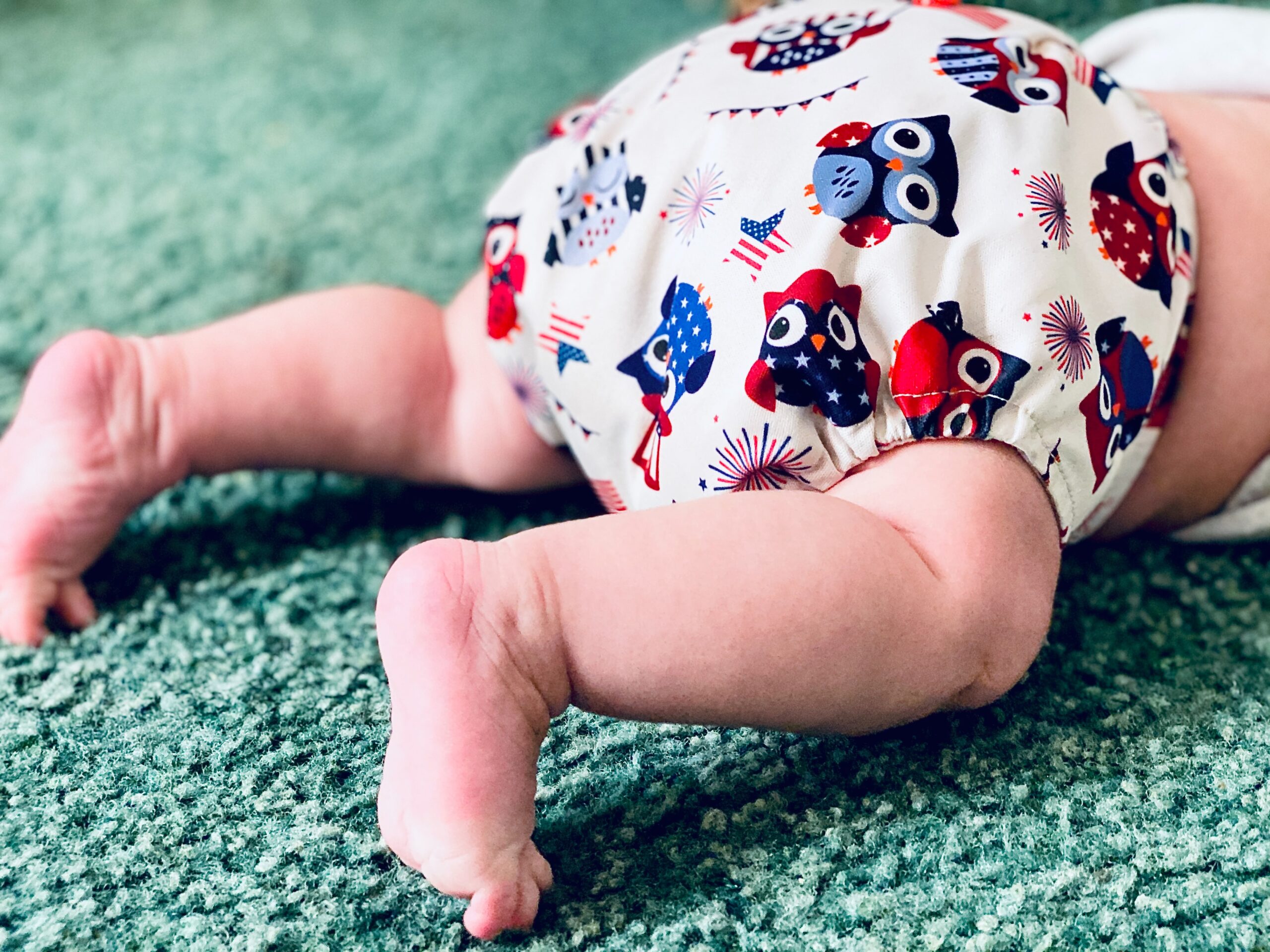 View of a baby's legs lying face down on a green carpet and wearing a reusable nappy