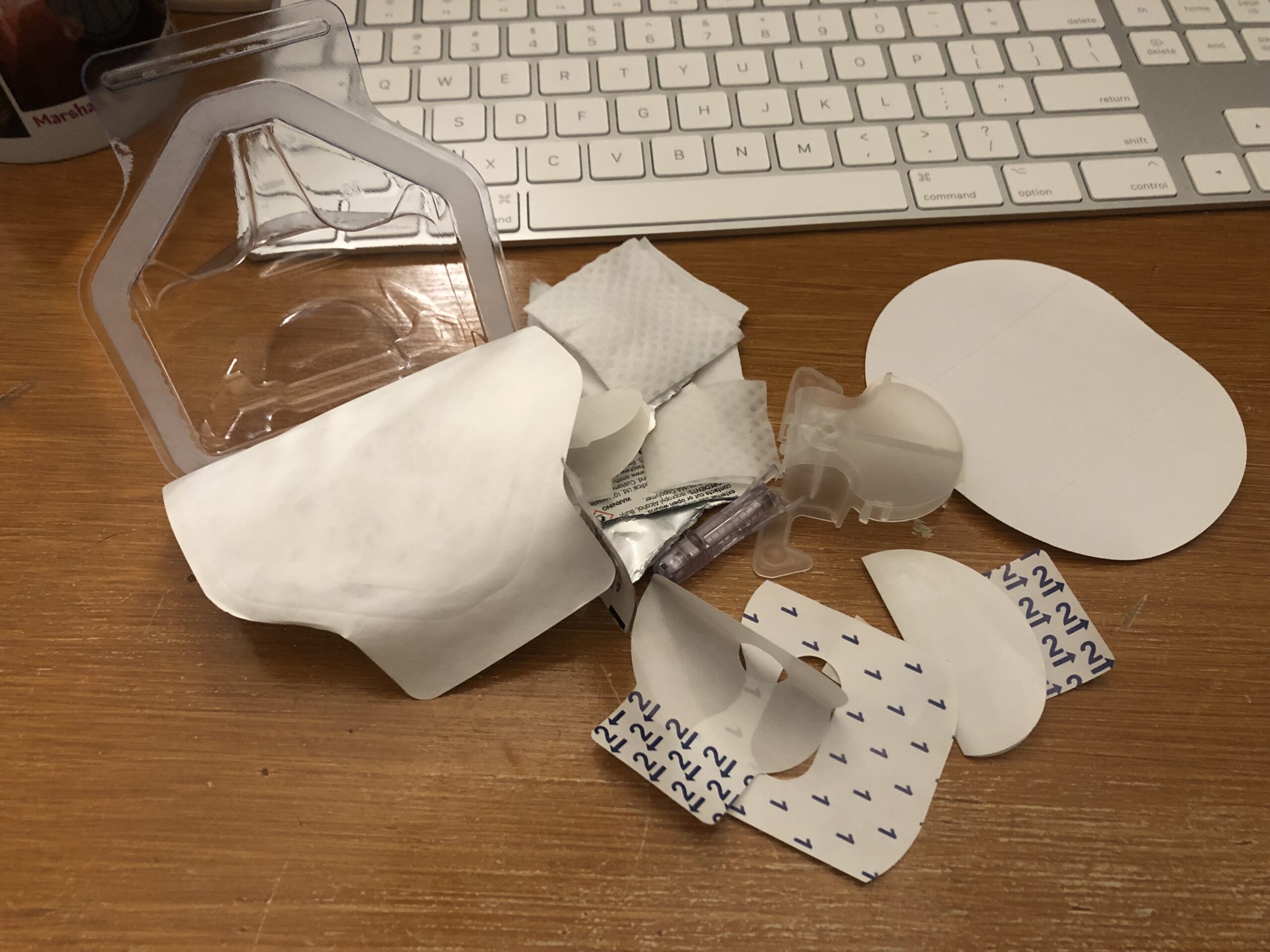 Elaborate plastic packaging from a continuous glucose monitor laid out on a wooden desktop