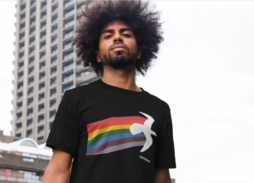 A model wears a black greenpeace tshirt with a rainbow design in an urban setting