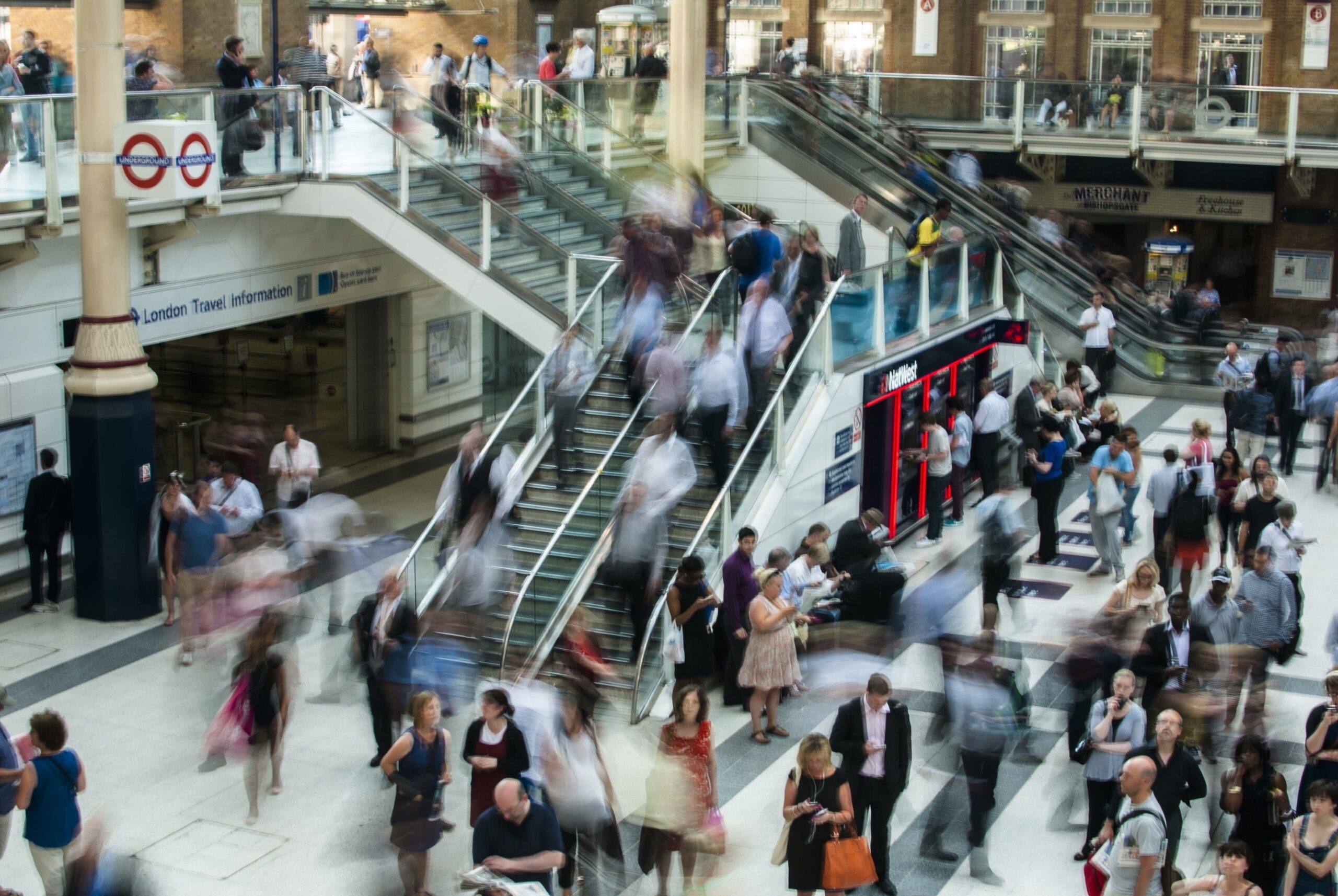 A busy station concourse viewed from above. Fast-moving pedestrians are motion-blurred.