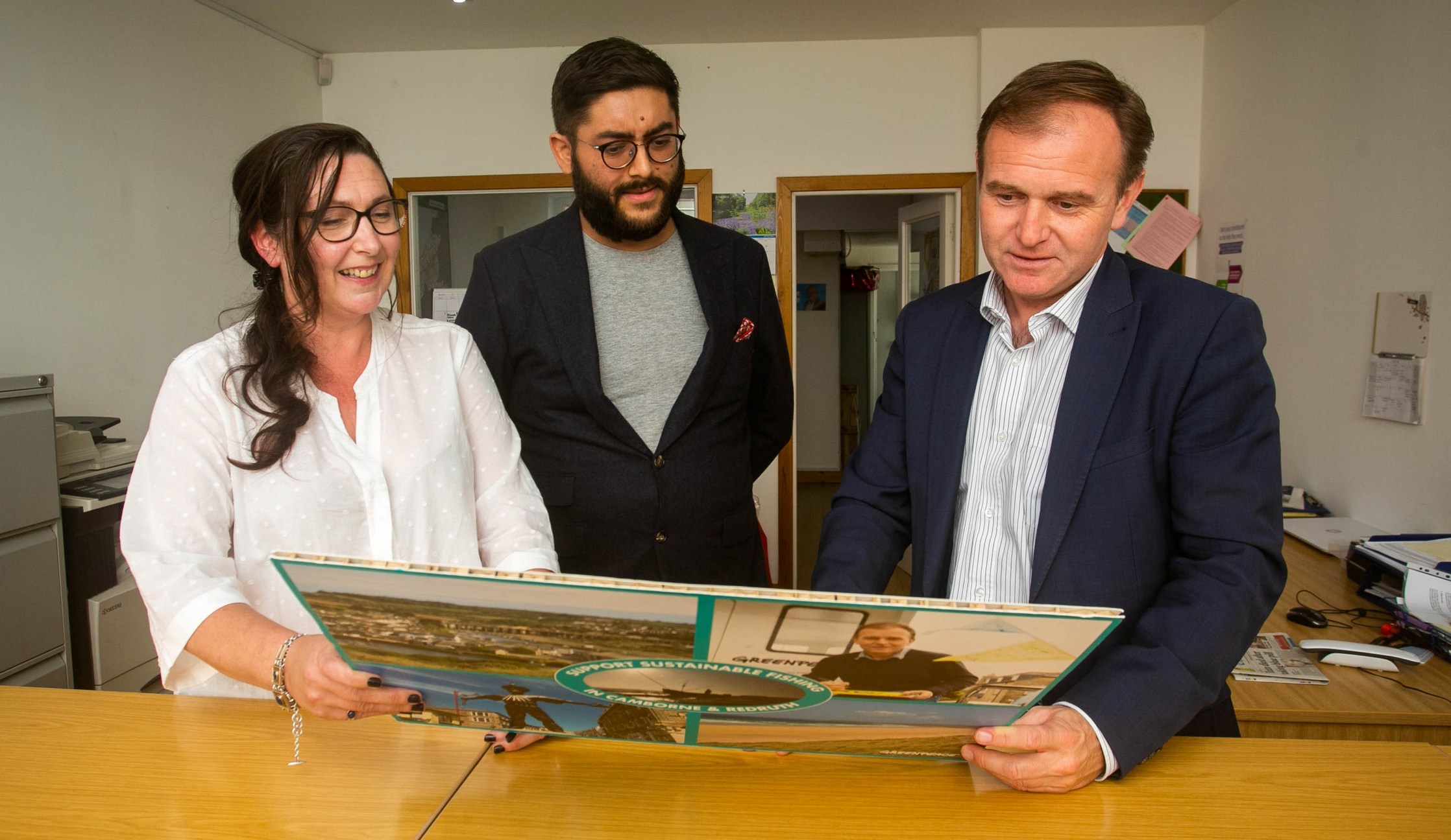 Accompanied by a Greenpeace campaigner, George Eustice looks at an oversized display board with sustainable fishing messages.