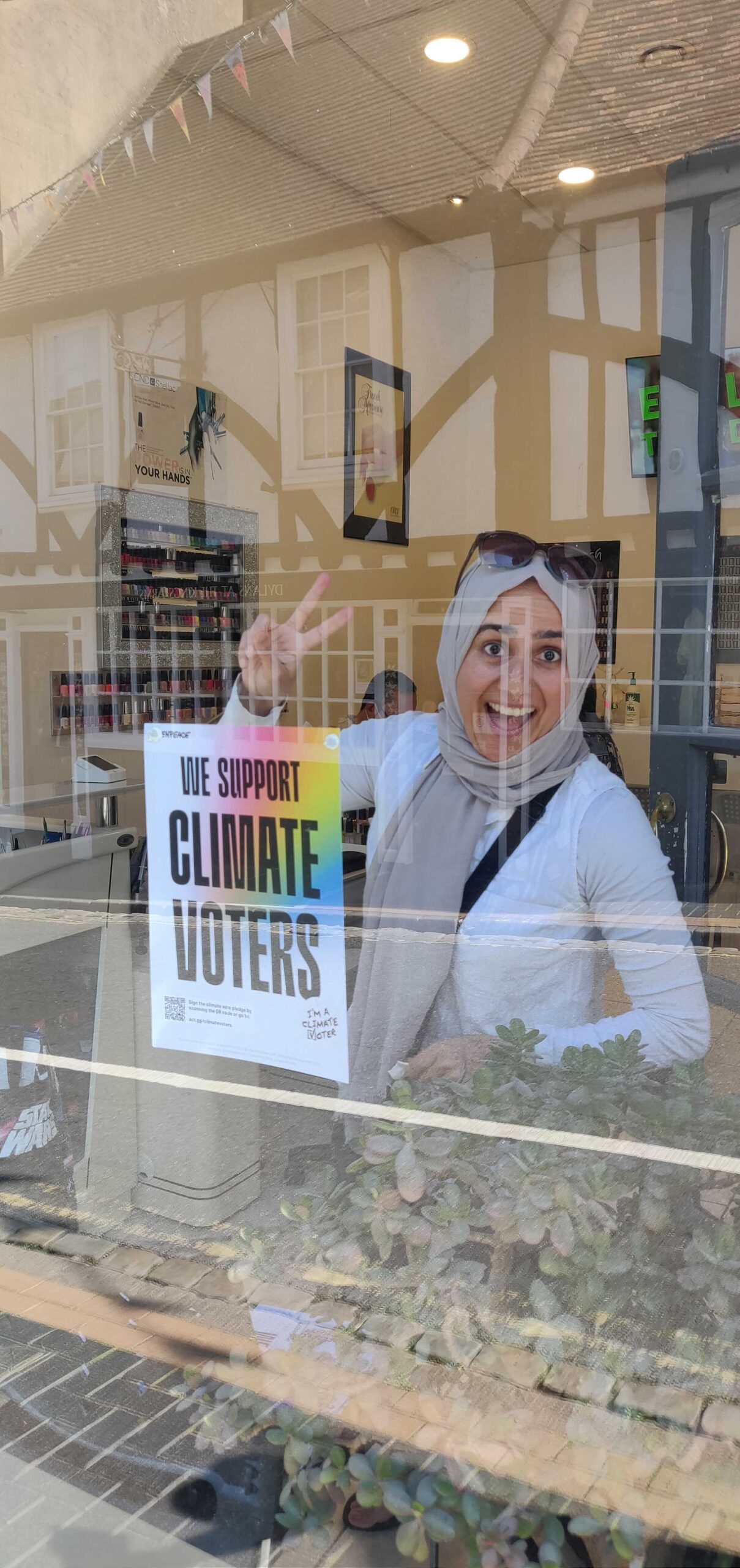 Woman behind a window throws up a peace sign with her climate vote poster