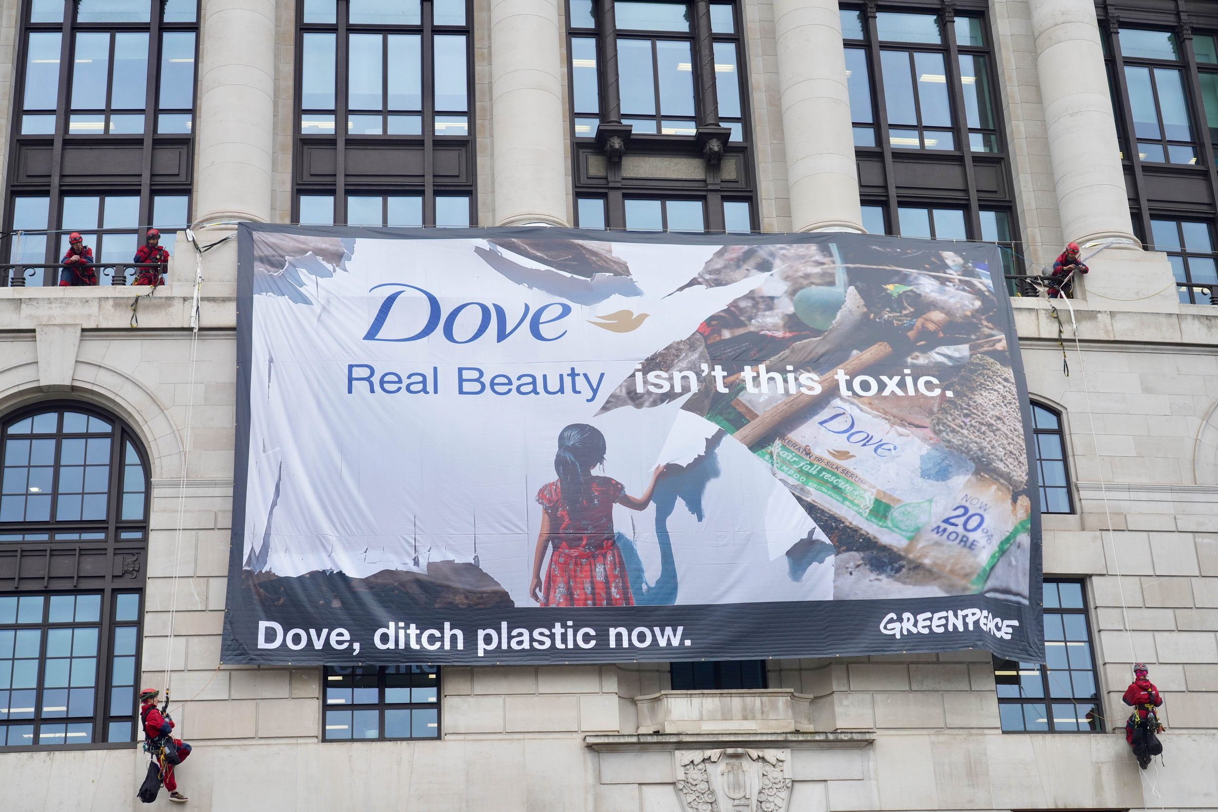A giant banner hangs from the grand stone building. It shows Dove plastic pollution with the wording "Real Beauty isn't this toxic. Dove, ditch plastic now"