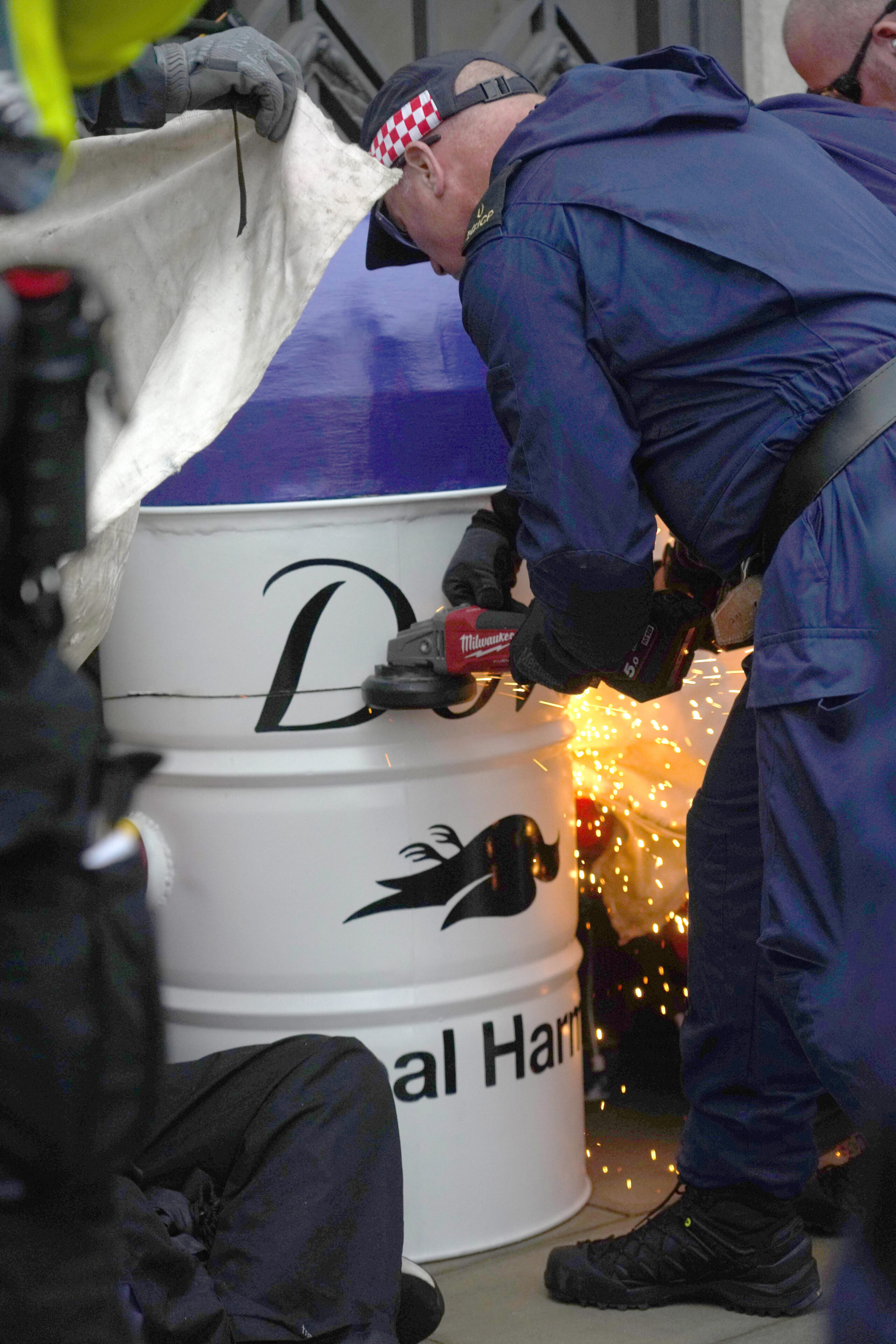 Sparks fly from an angle grinder as police cut an activist free from a large model of a Dove deodorant container.
