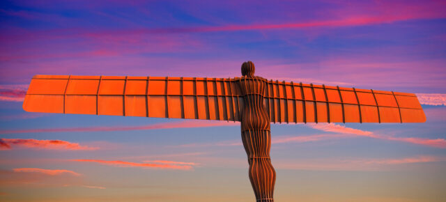 The Angel of the North, a giant metal sculpture, spreads its wings against a beautiful sunset.