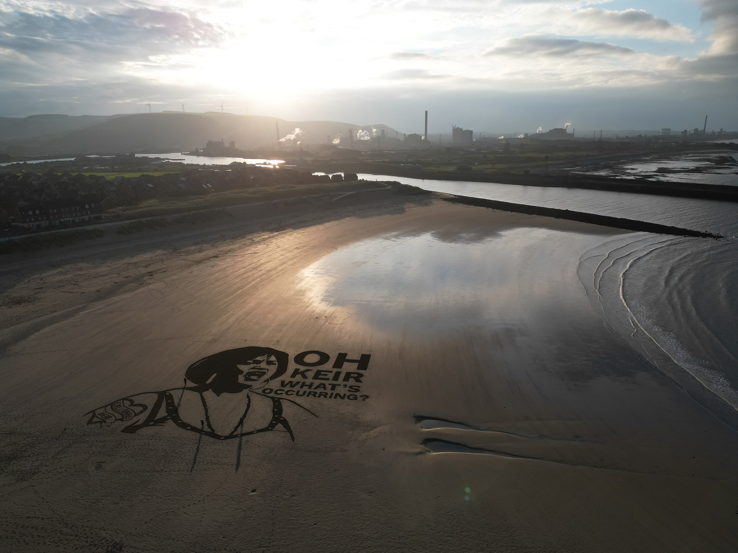 Atmospheric aerial shot of sand art showing the face of character Nessa from the TV series Gavin & Stacey with the sentence 'Oh Keir What's occurring?' next to the face.