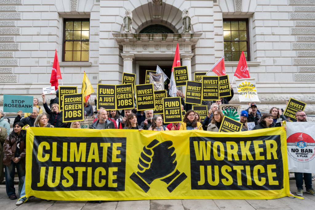 Activists with a yellow and black banner and placards stand in front of the Treasury building. The banner says 'Climate Justice Worker Justice'