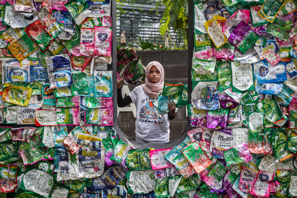 An activist stands in the middle of a big U that is created with single use plastic by the company Unilever.