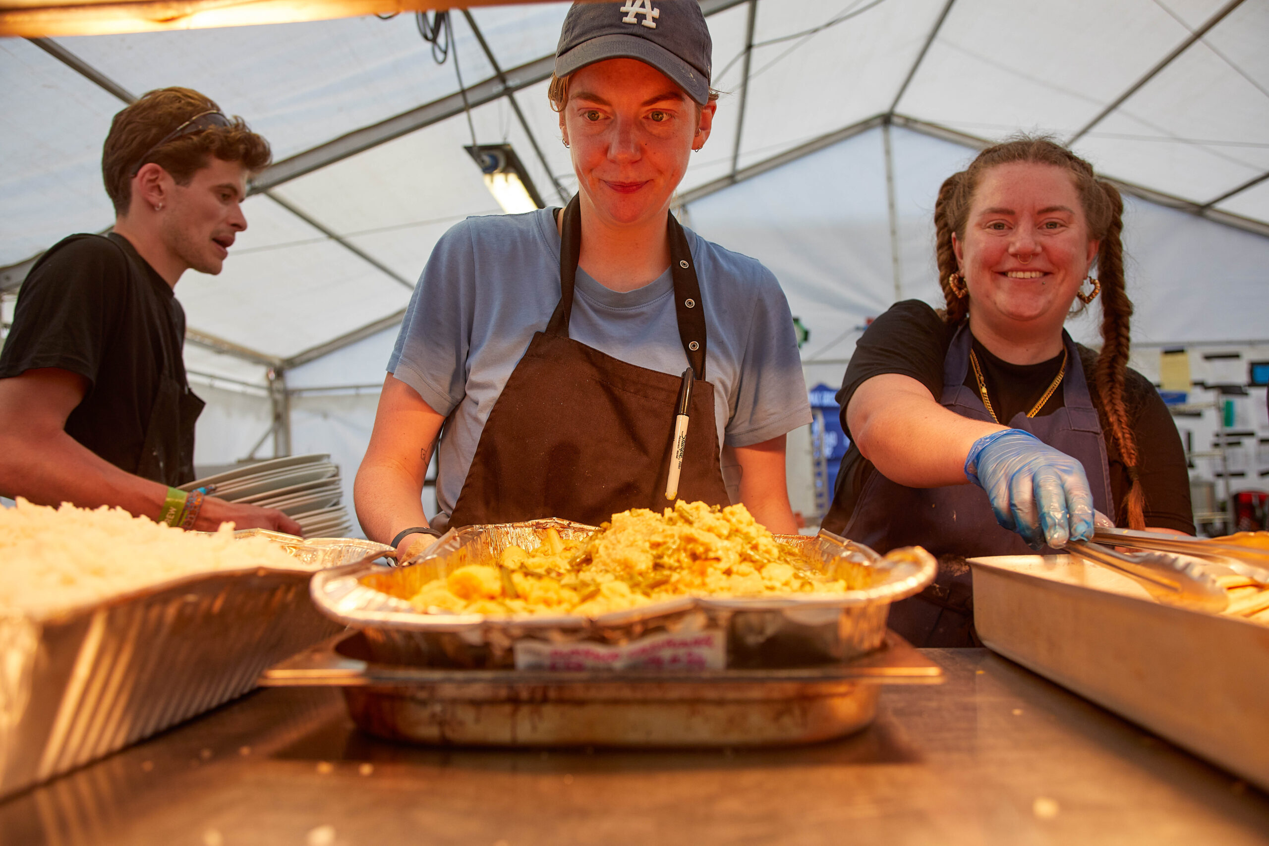 A person serves food over a counter in a big marquee