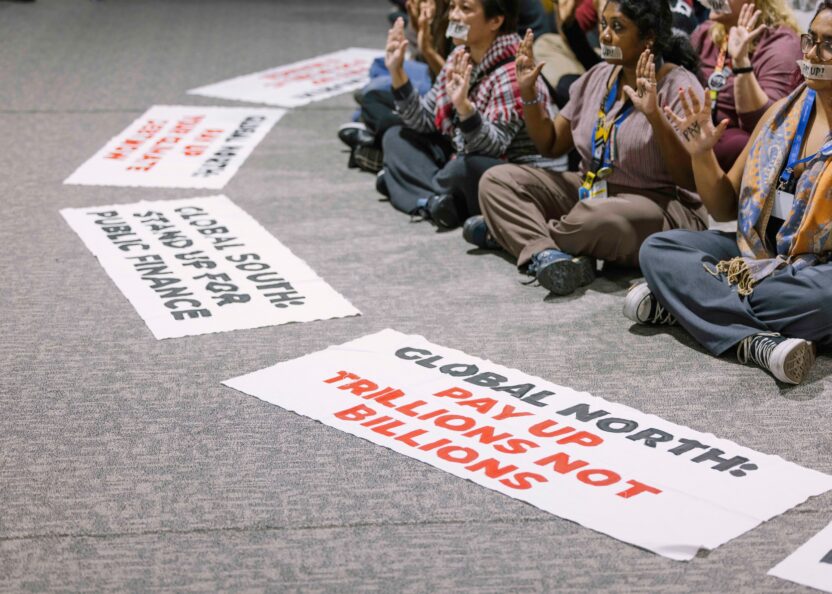 Activists in a sit-down protest with signs calling for better climate finance and loss and damage funding.