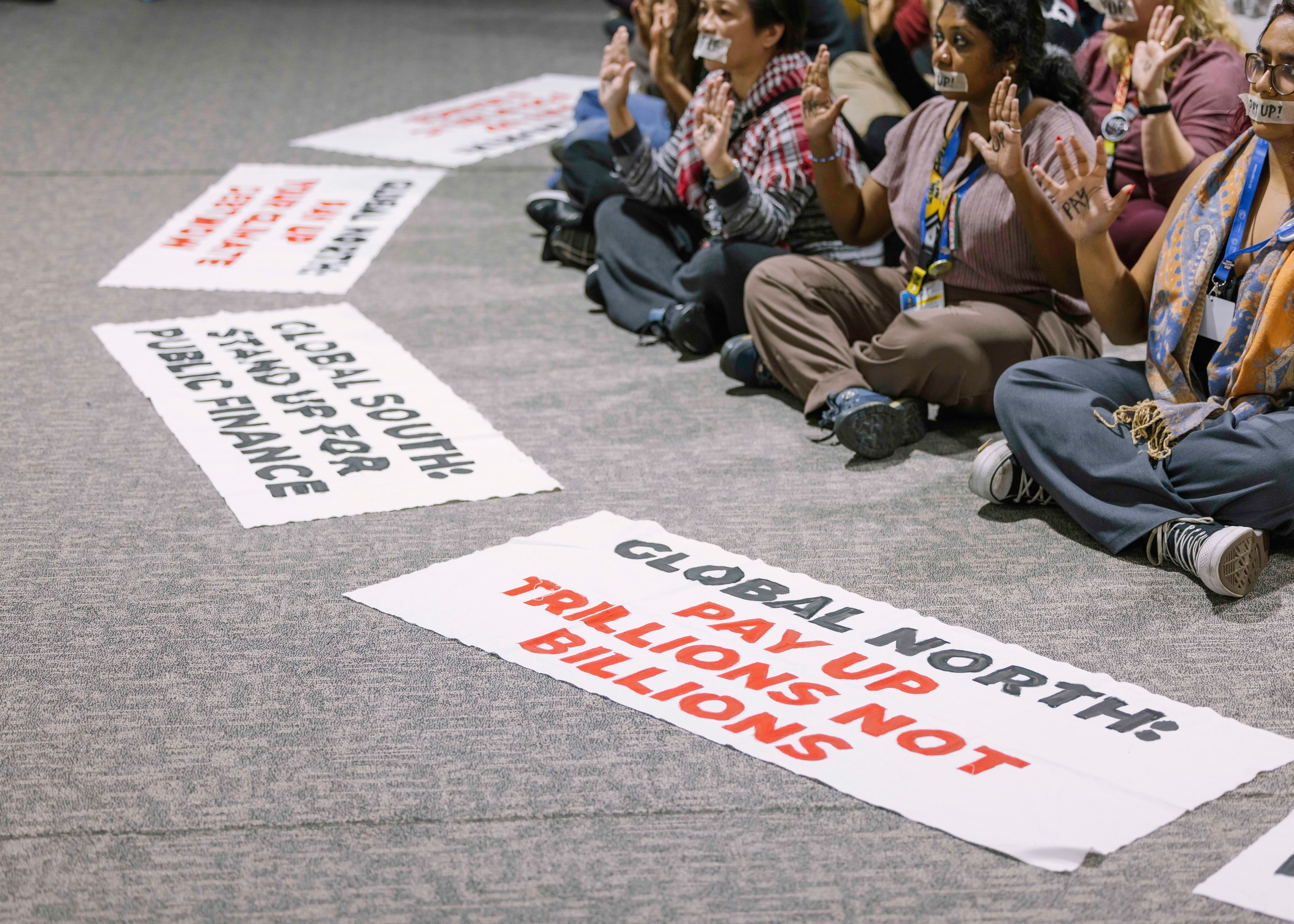 Activists in a sit-down protest with signs calling for better climate finance and loss and damage funding.