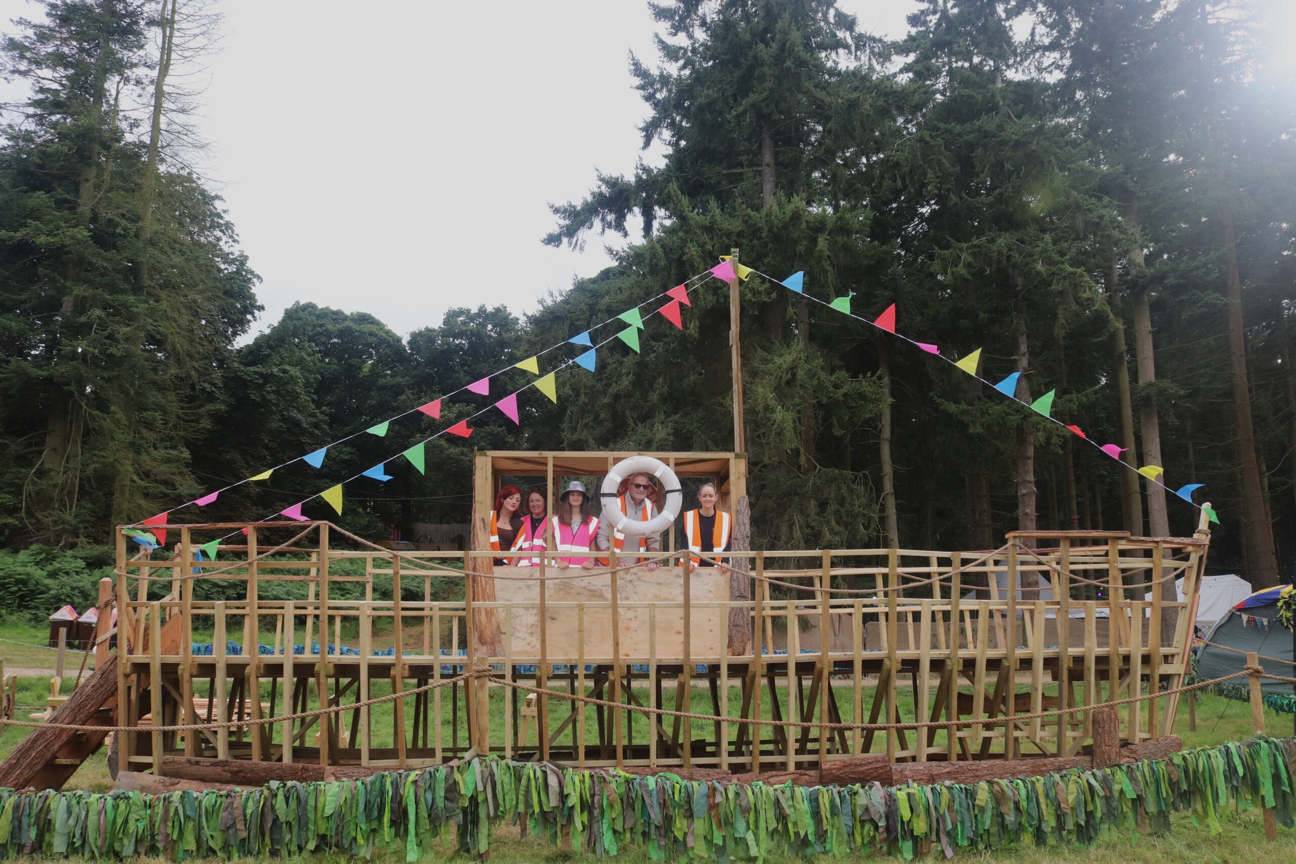 Greenpeace volunteers stand on a large wooden boat structure with trees in the background