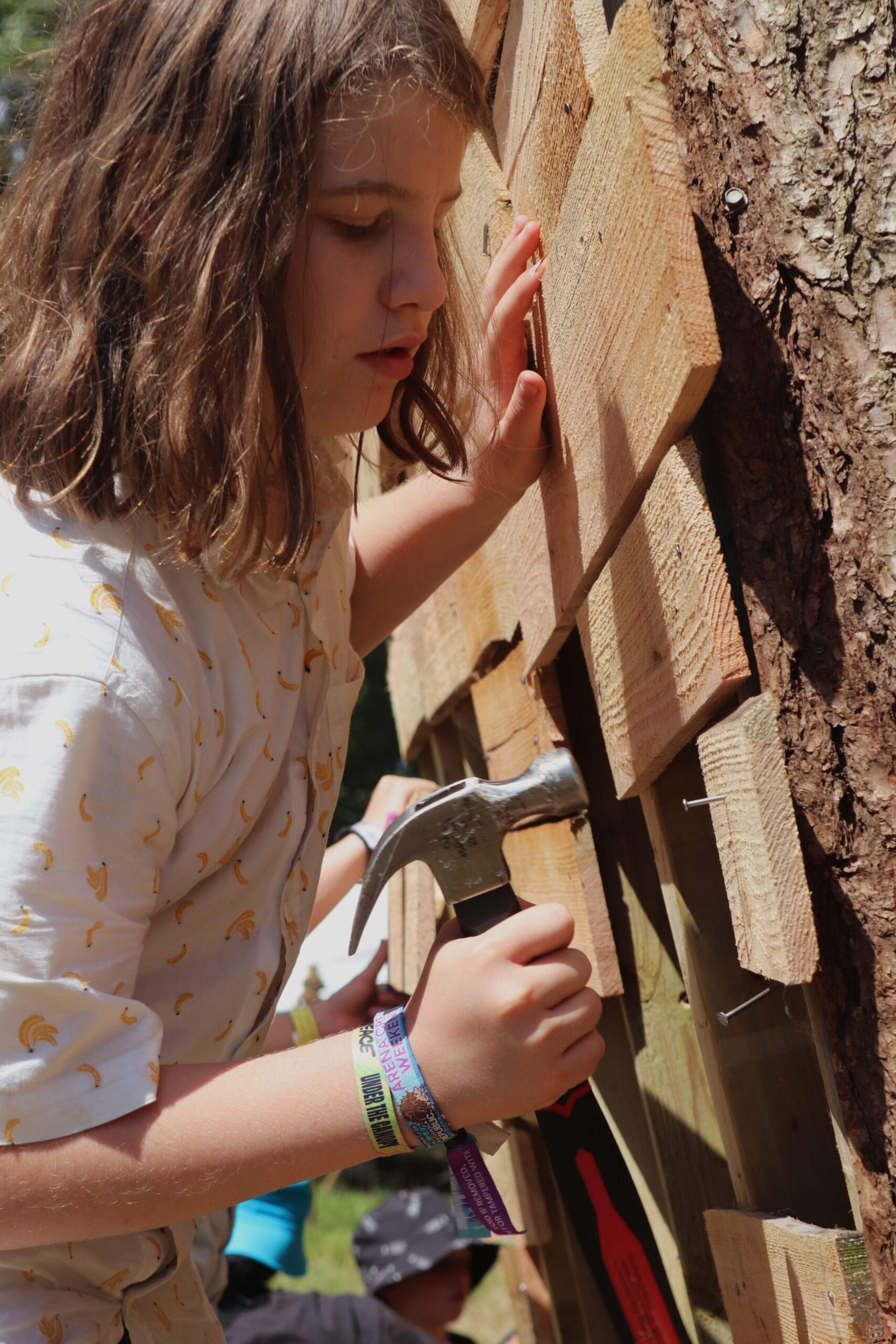 A girl uses a hammer to knock nails into a piece of wood