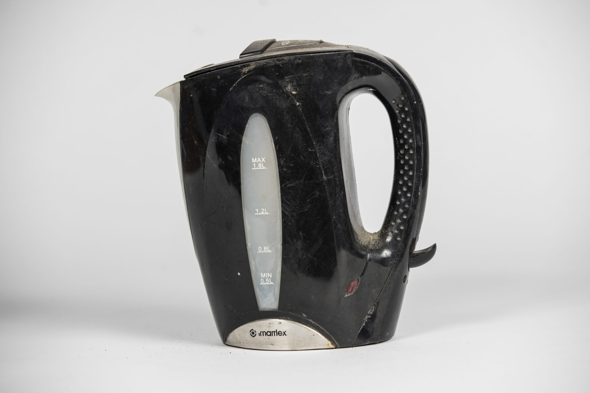 A black kettle with stains from floodwater stands against white background