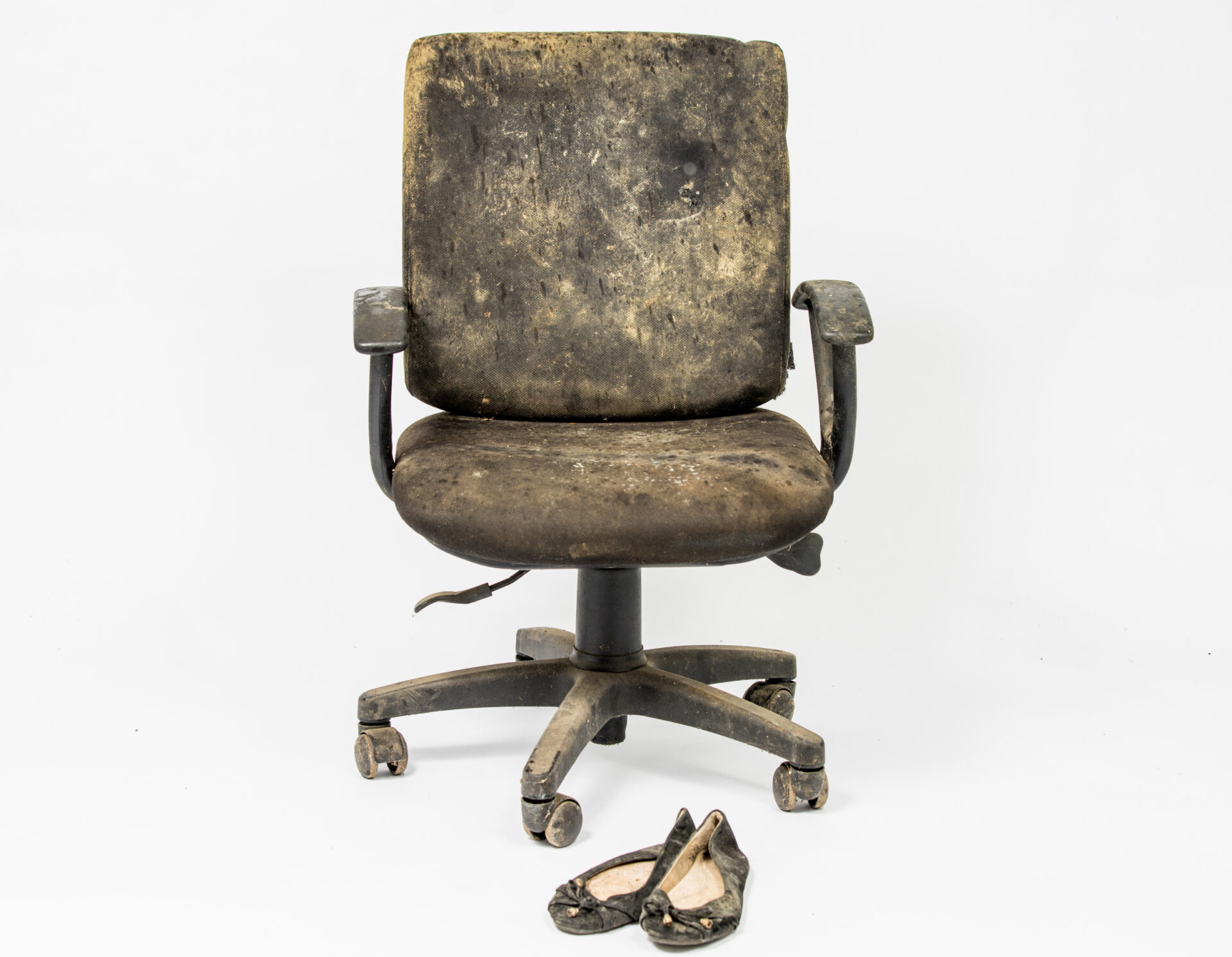 An office chair with stains from flood waters is photographed against a white background, shoes are placed on the floor in front.
