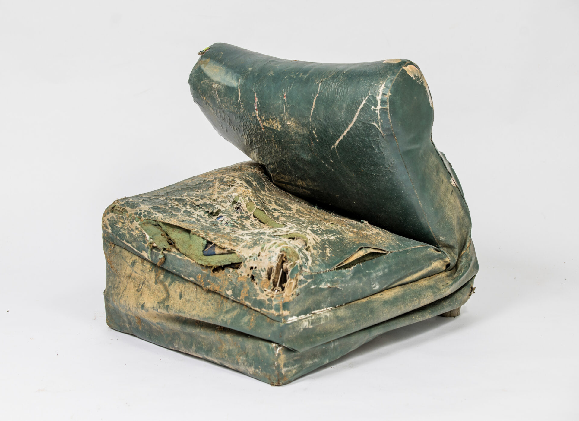A green broken chair, with holes and stains caused by flood waters is photographed against a neutral background