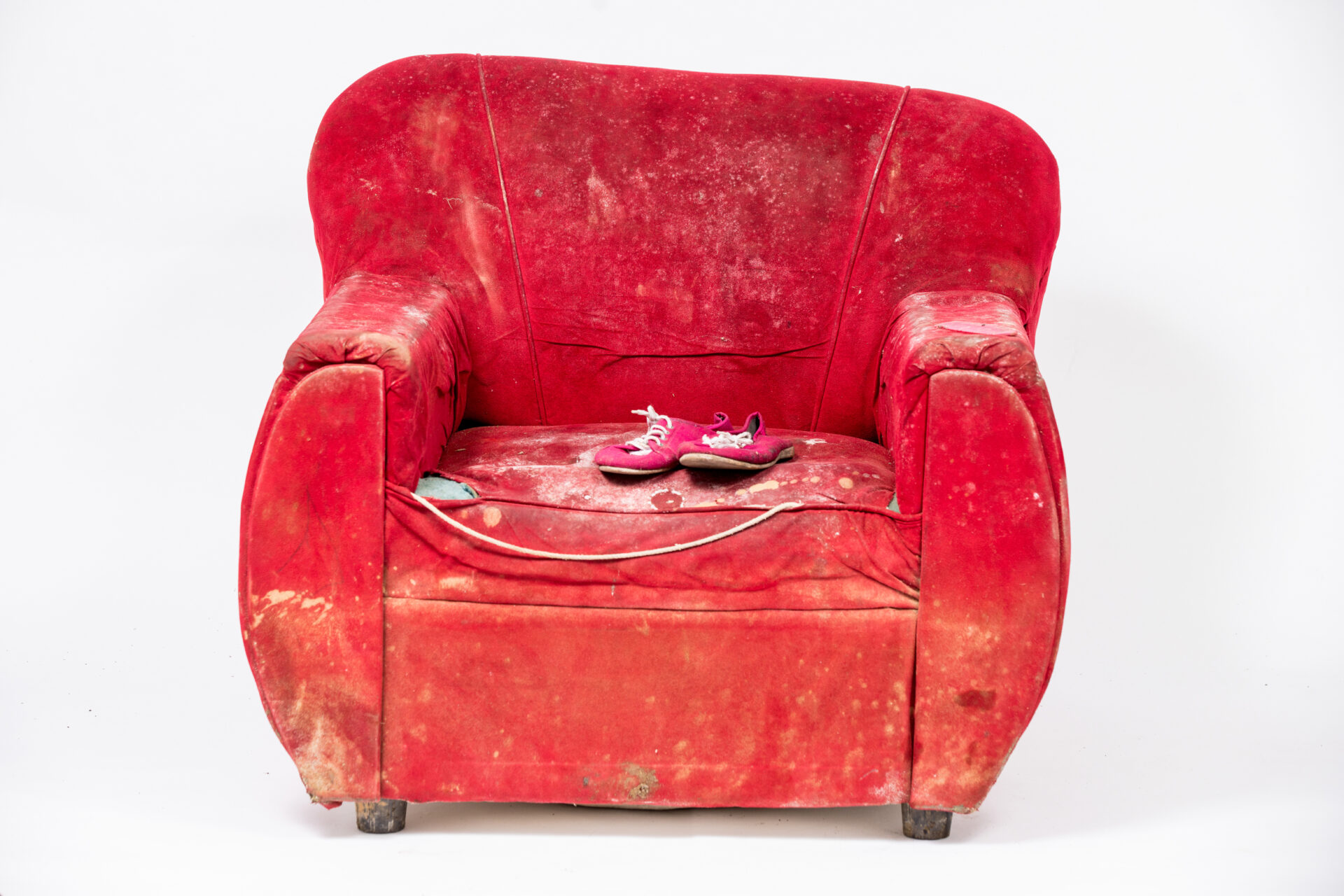 A red armchair with pink shoes on the seating area is photographed against a neutral background