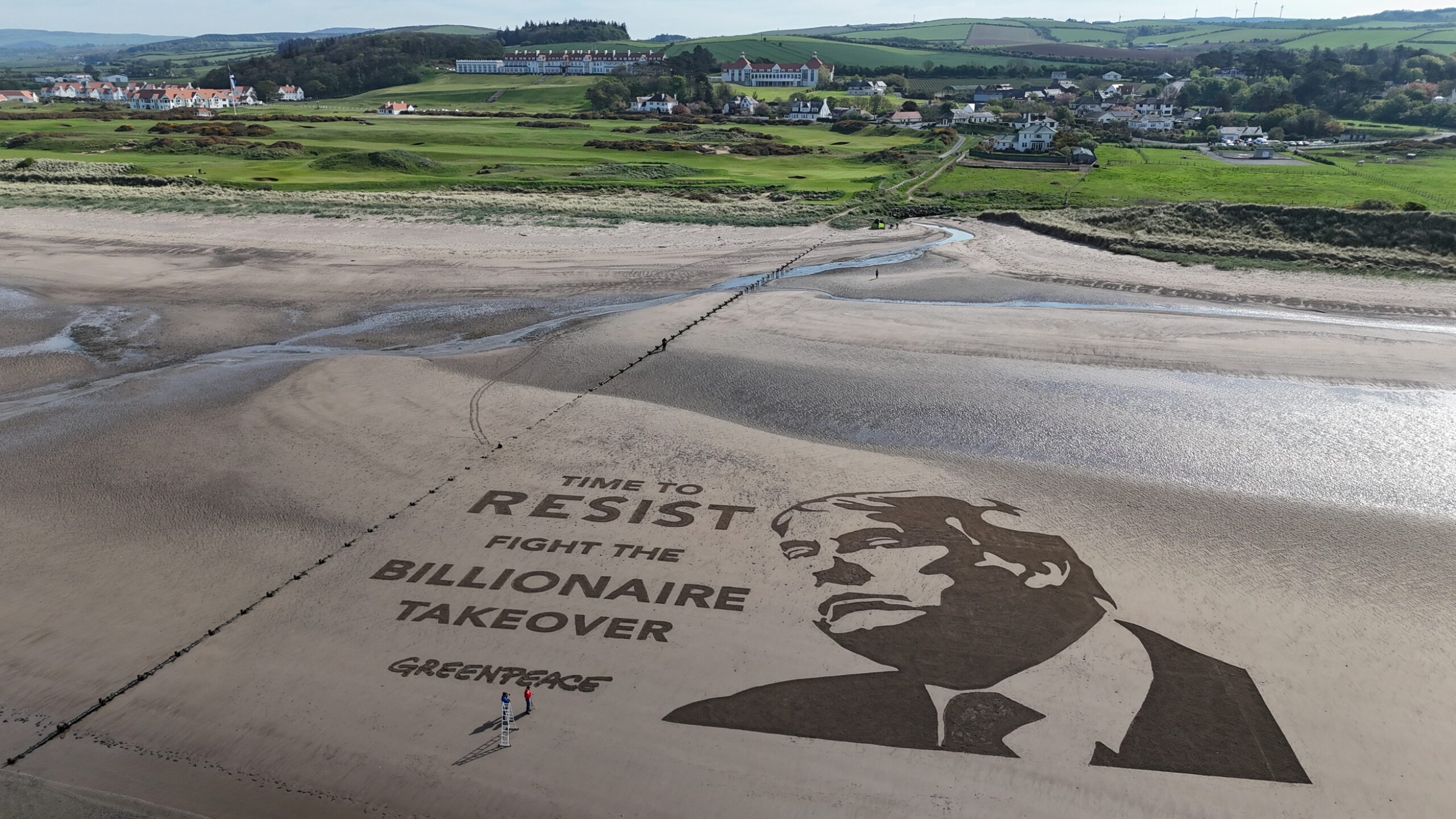 A giant sand artwork on a Scottish beach features a portrait of Donald Trump alongside the words “TIME TO RESIST. FIGHT THE BILLIONAIRE TAKEOVER. GREENPEACE”. The artwork is located near a coastal golf resort.