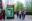 A Greenpeace billboard at a London bus stop near the US Embassy displays a green background with the face of Donald Trump, crossed out with a black line, and the words “TIME TO RESIST”. Passers-by walk past the scene in an urban setting.