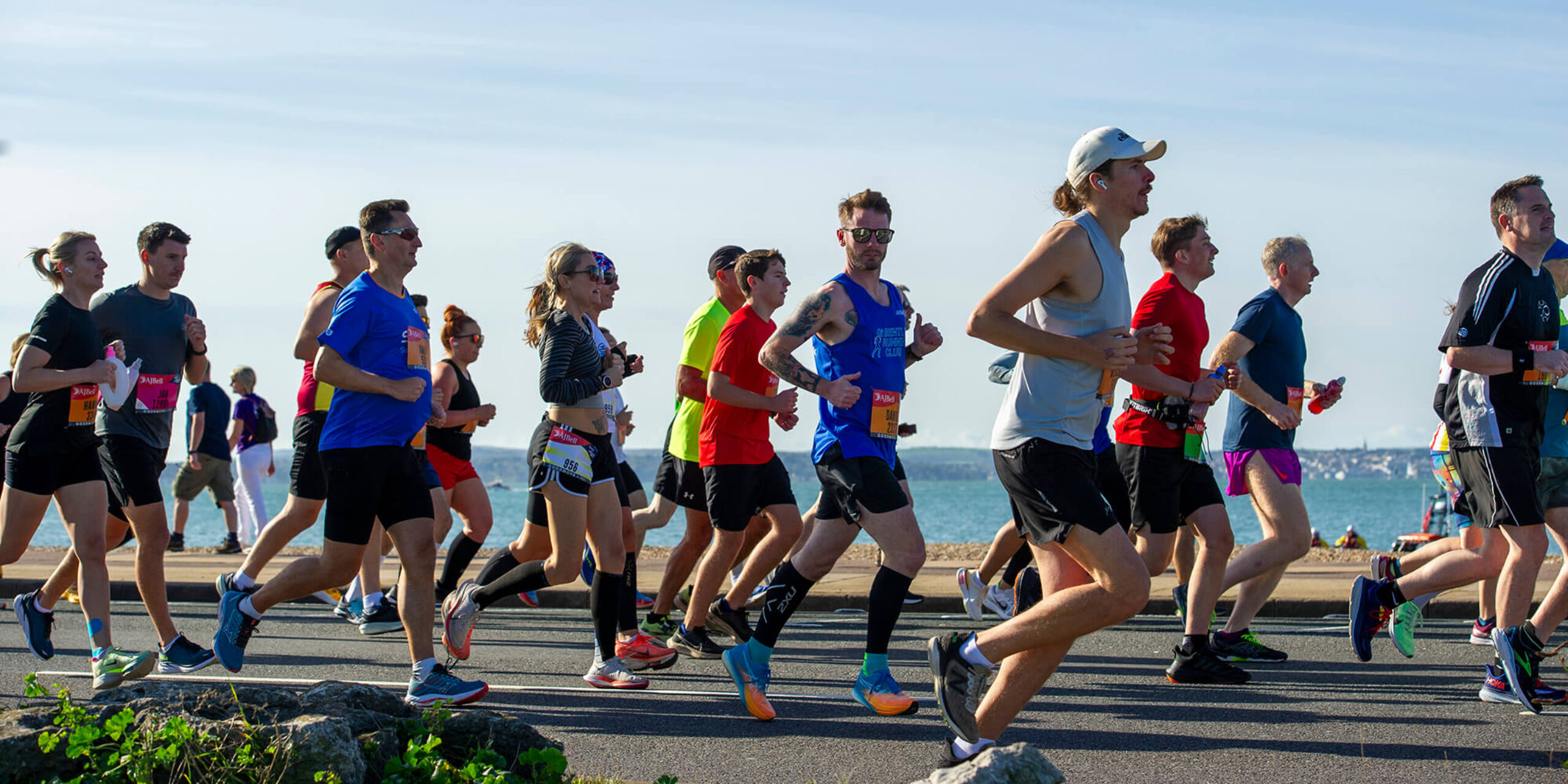A group of runners race along the coast in sunny weather with the sea and horizon in the background, during the Great South Run.