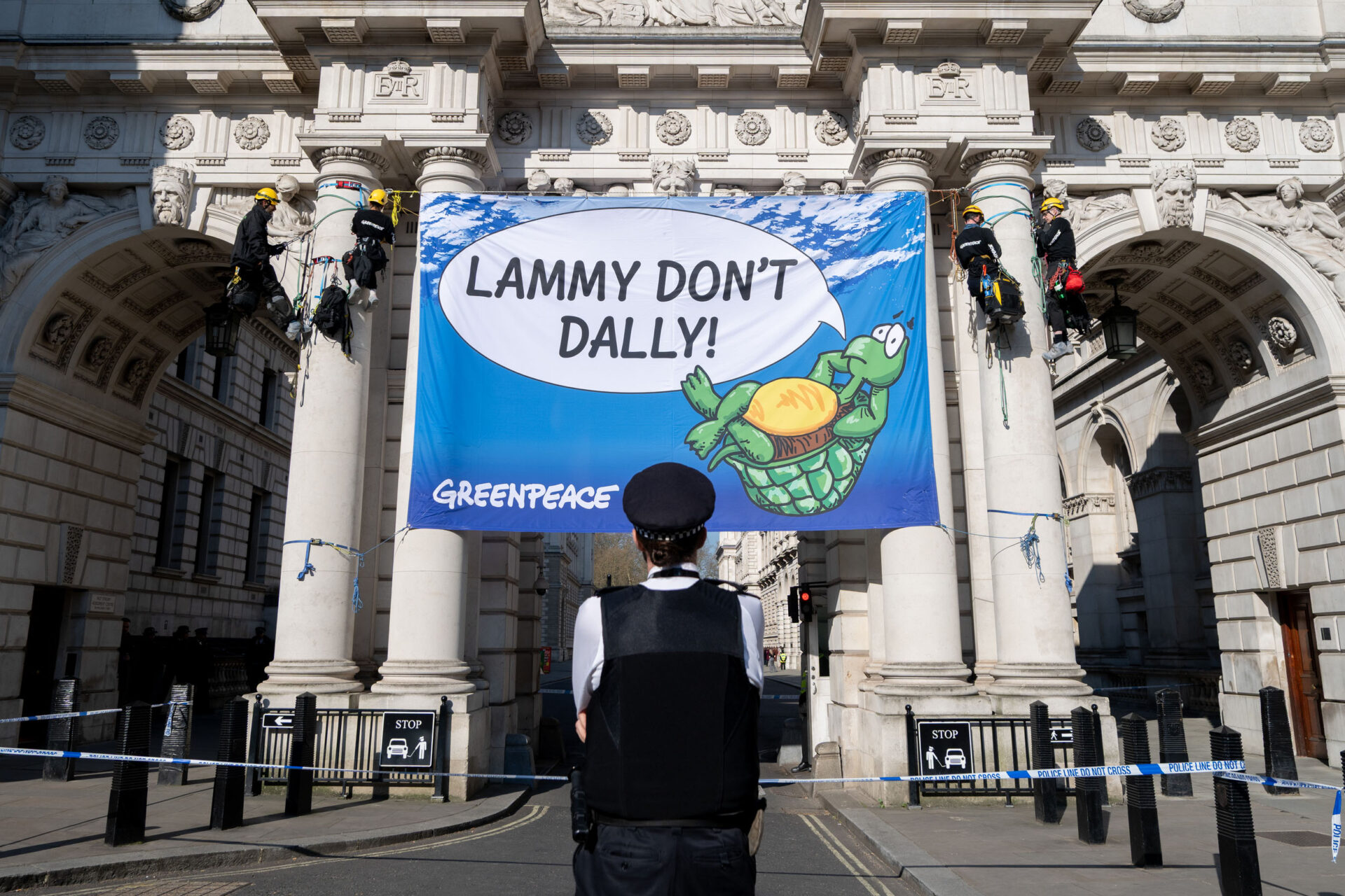 A policeman looks at a banner with a turtle and a speech bubble saying "Lammy Don't Dally".