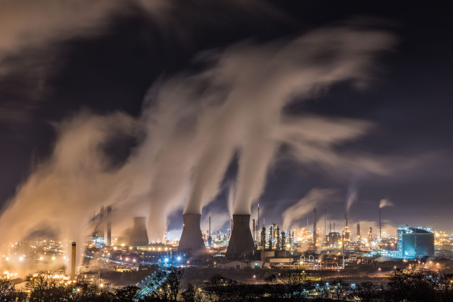 Night-time view of an oil refinery with smoke arising.
