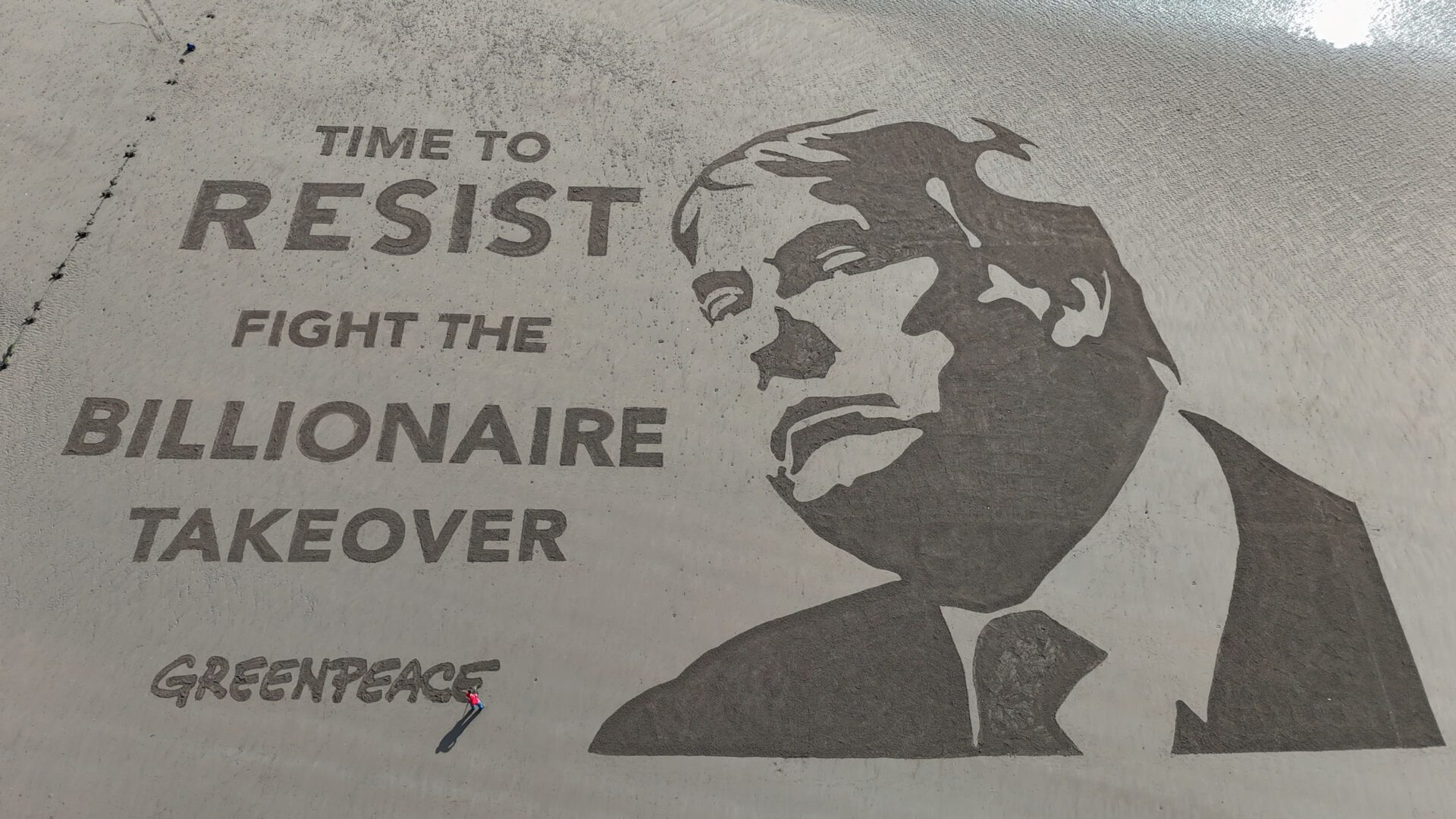 Aerial view of a sandart image of Donald Trump and writing saying: "Time to Resist. Fight the Billionaire Takeover".