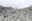 A huge heap of waste can be seen in the foreground with a tiny person standing in the background on top.