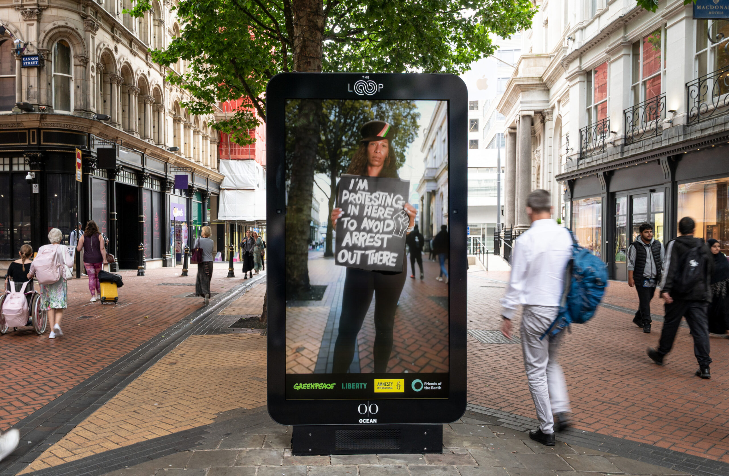 A protester on an electronic ad screen holds a sign saying 'I'm protesting in here to avoid arrest out there.'