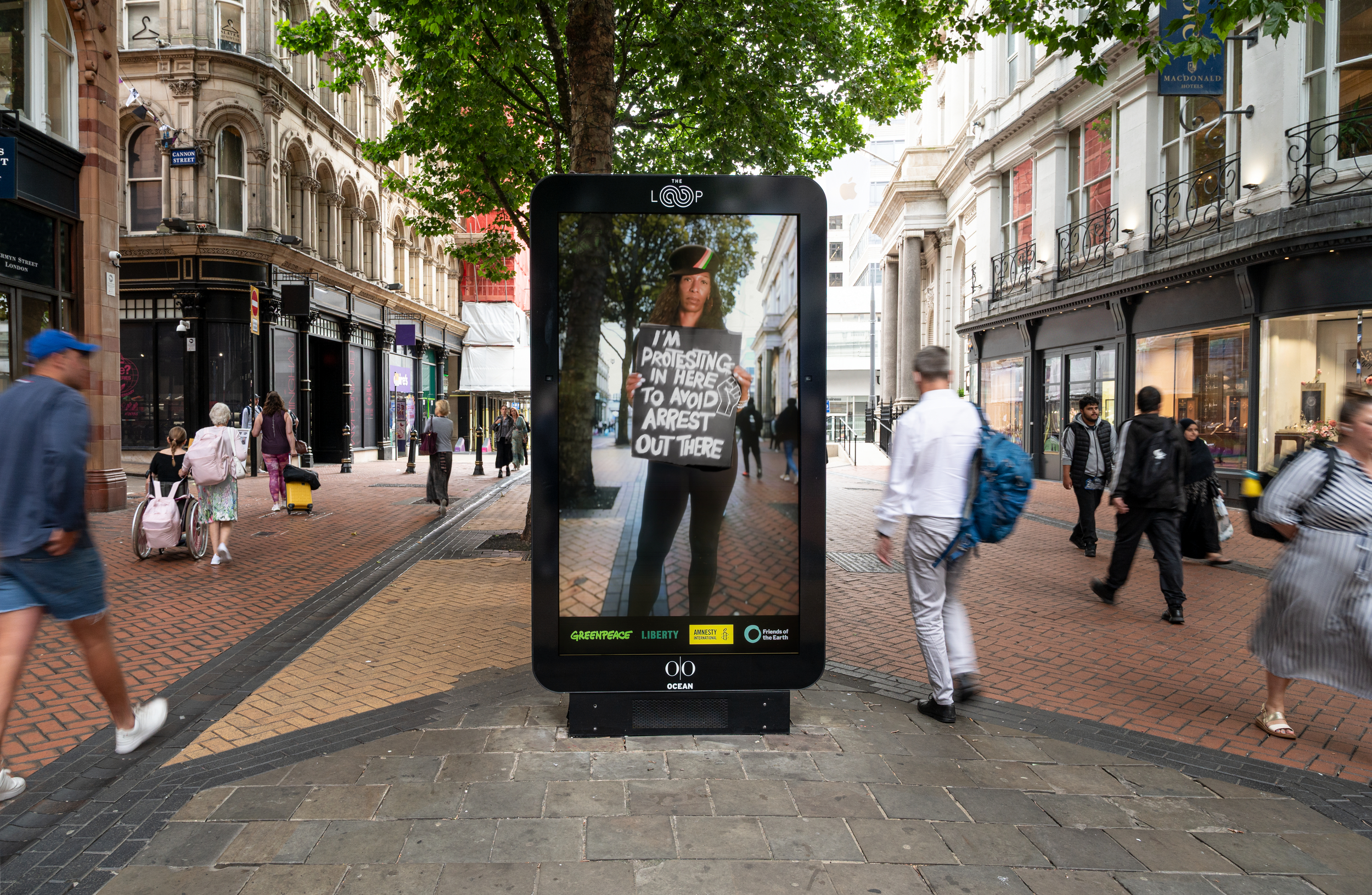 A protester is pictured holding a placard in a billboard on a shopping street in Birmingham as people walk past