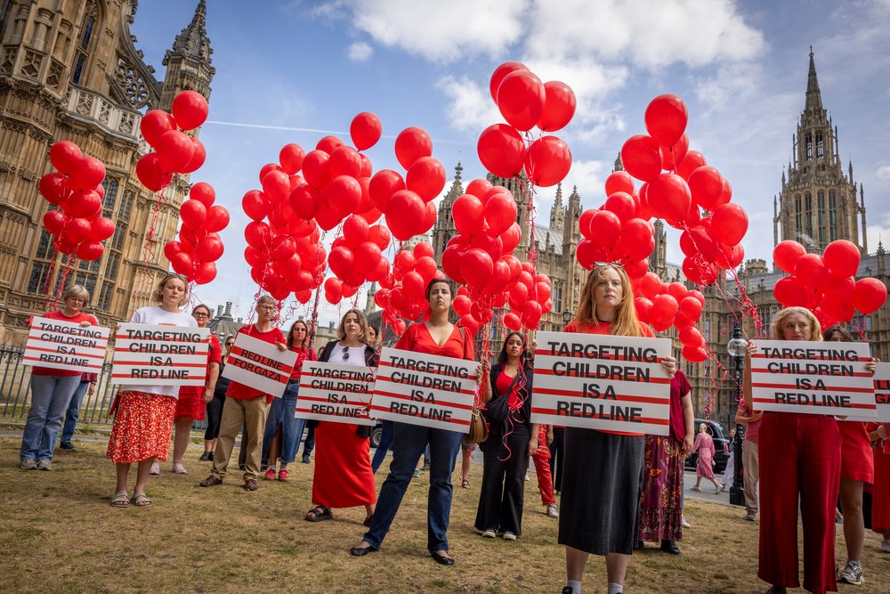 People with red balloons and signs saying 'Targeting children is a red line'