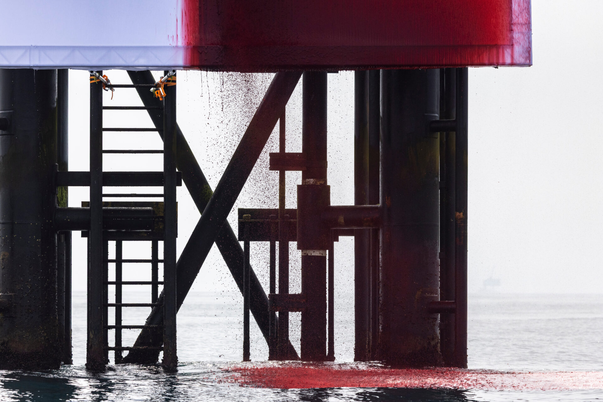 Fake blood drips off a giant white fabric backdrop attached to an offshore platform in a calm ocean.