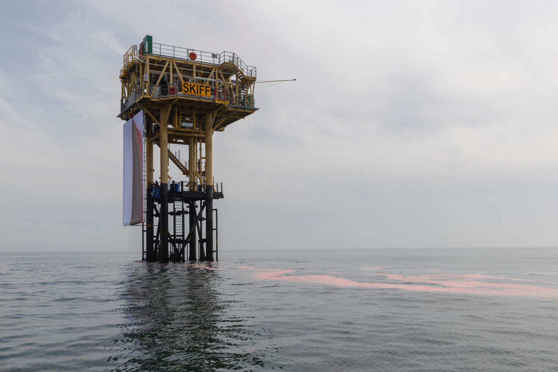 Fake blood stains a giant white fabric backdrop attached to an offshore platform in a calm ocean.